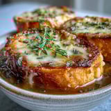 A close-up of classic French Onion Soup showing caramelized onions and cheesy bread in rich broth.