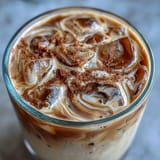 Iced brown sugar oat milk shaken espresso in a tall glass with ice and frothy oat milk.