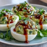 Vibrant deviled eggs filled with avocado-lime mash, topped with fiery Sriracha and fresh cilantro for a zesty twist.