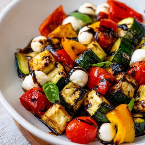 Roasted Veggie Caprese Salad features caramelized zucchini, peppers, and tomatoes topped with mozzarella pearls and fresh basil.