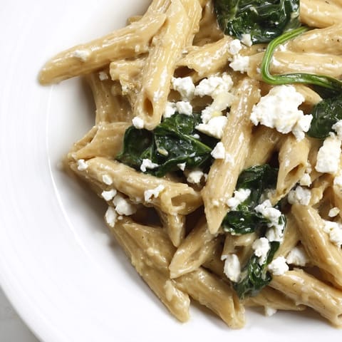 Close-up of Creamy Feta Spinach Pasta, with fresh basil and lemon zest garnish on a rustic wooden table.