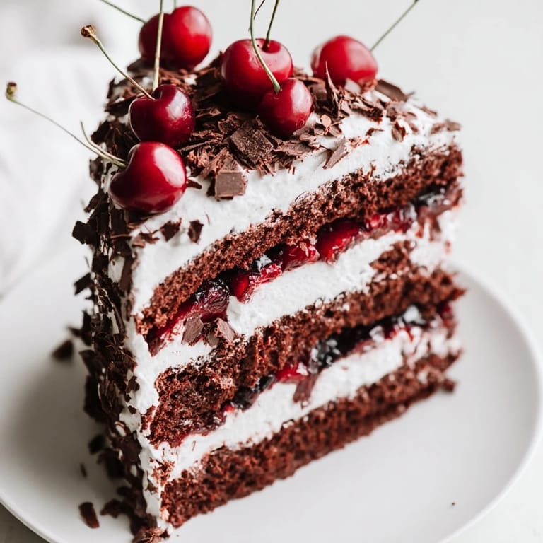 A close-up of a slice of Black Forest Cake features rich chocolate and cherry filling.