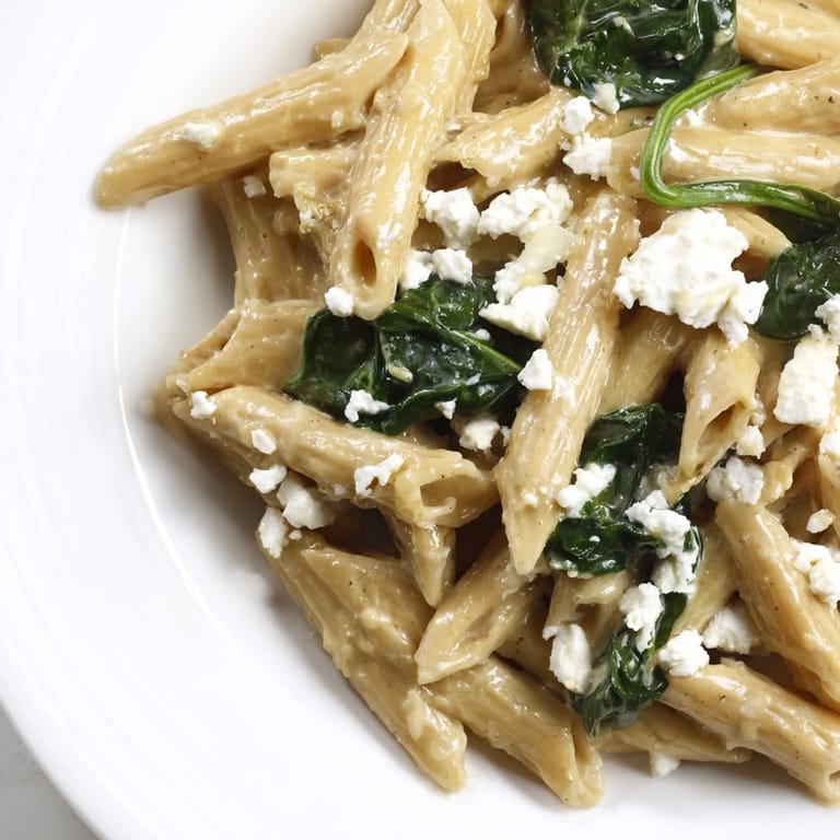 Close-up of Creamy Feta Spinach Pasta, with fresh basil and lemon zest garnish on a rustic wooden table.