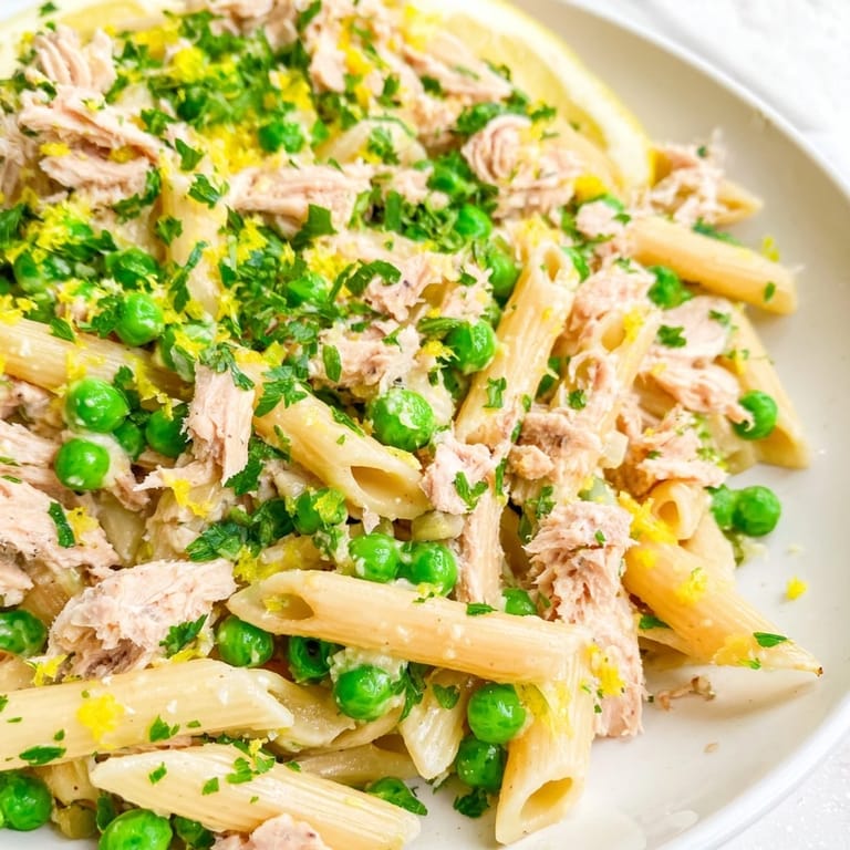 Ready-to-serve Lemony Tuna Pasta Salad for picnics and lunches, featuring sweet peas, briny capers, and chopped parsley garnish.